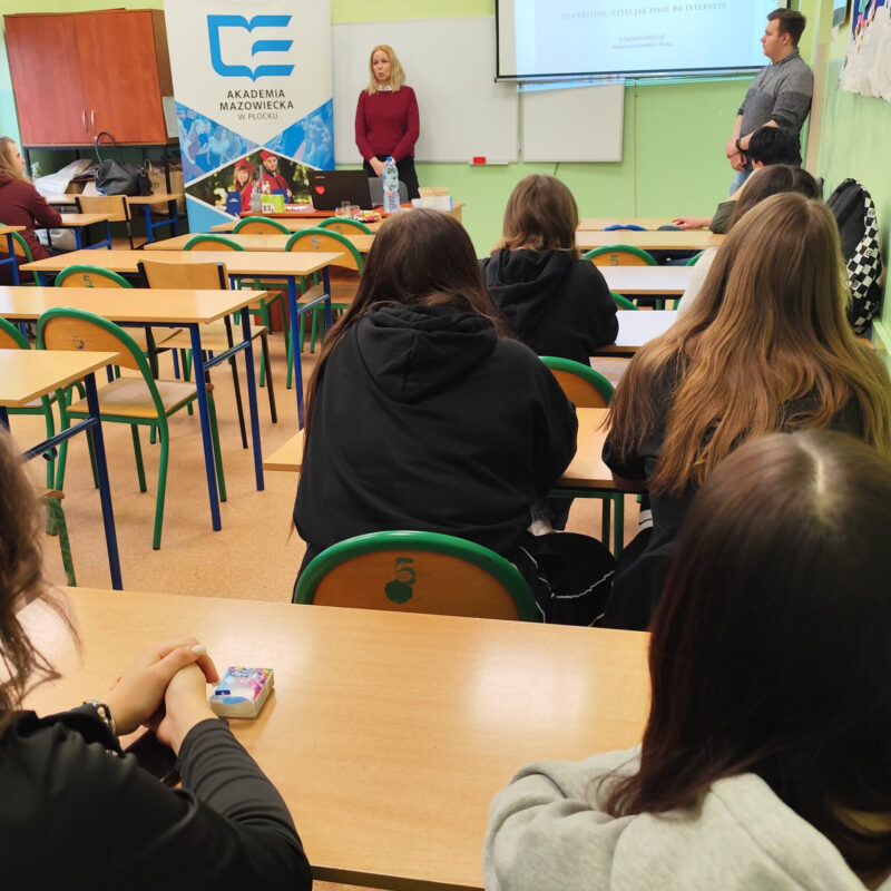 Nauczycielka akademicka omawiająca prezentację z podstaw webwritingu przed uczniami siedzącymi w ławkach szkolnych