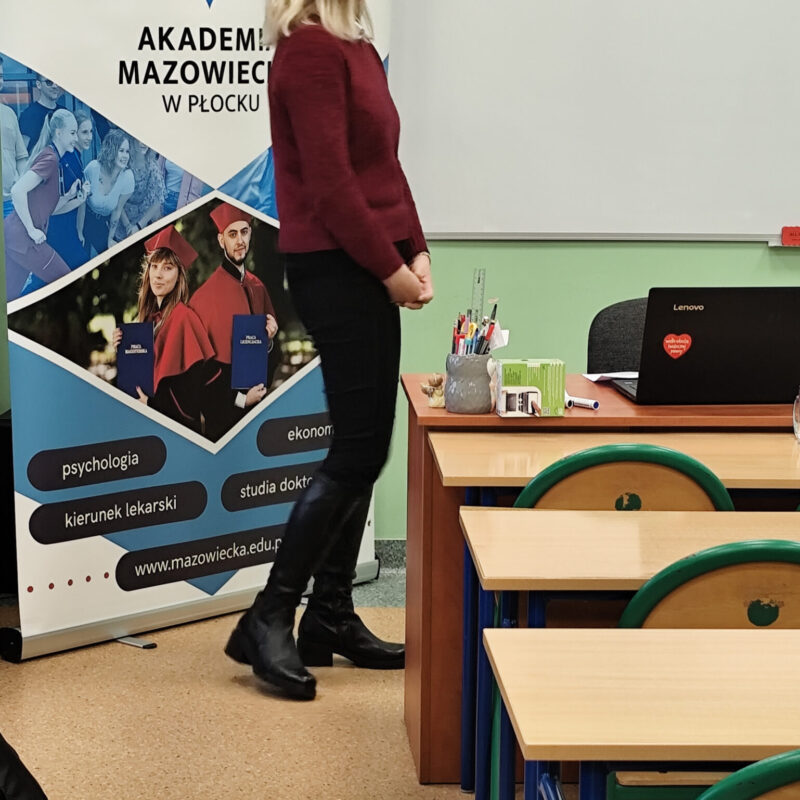 Nauczycielka akademicka omawiająca prezentację z podstaw webwritingu przed uczniami siedzącymi w ławkach szkolnych