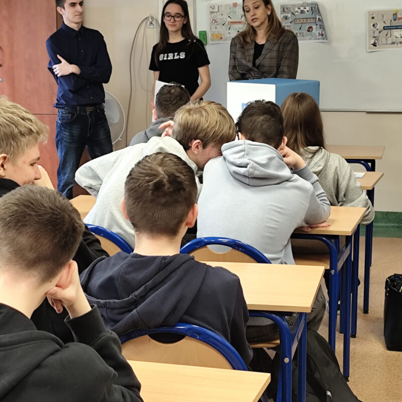 Nauczycielka akademicka omawiająca prezentację z podstaw ekonomii przed uczniami siedzącymi w ławkach szkolnych