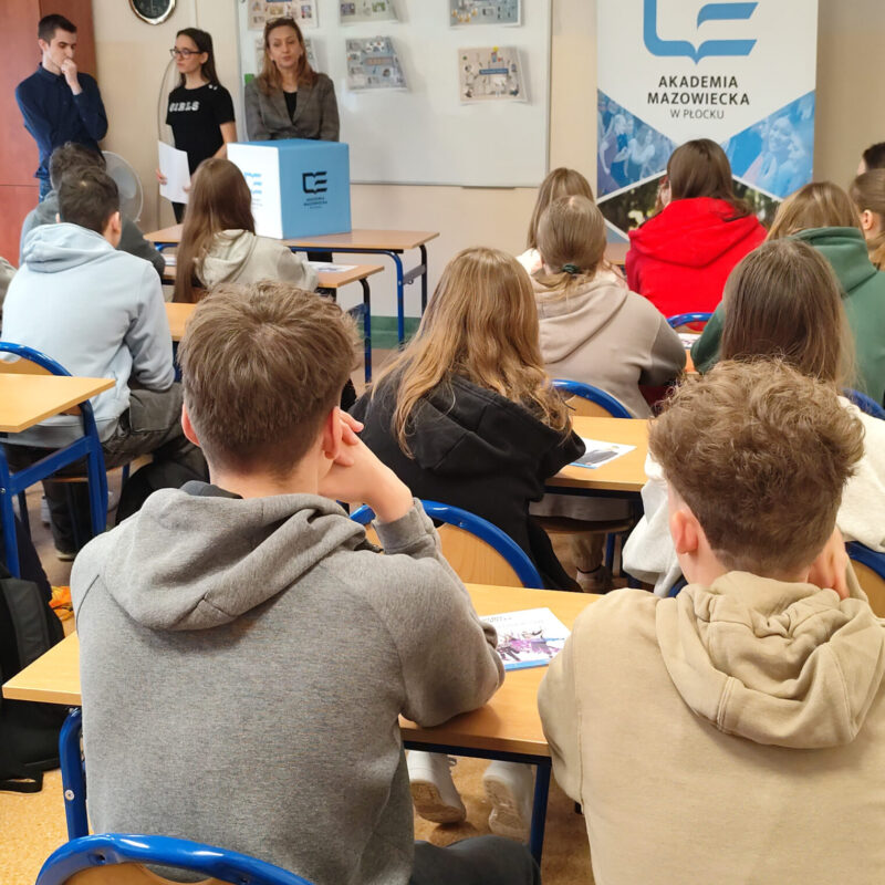 Nauczycielka akademicka omawiająca prezentację z podstaw ekonomii przed uczniami siedzącymi w ławkach szkolnych