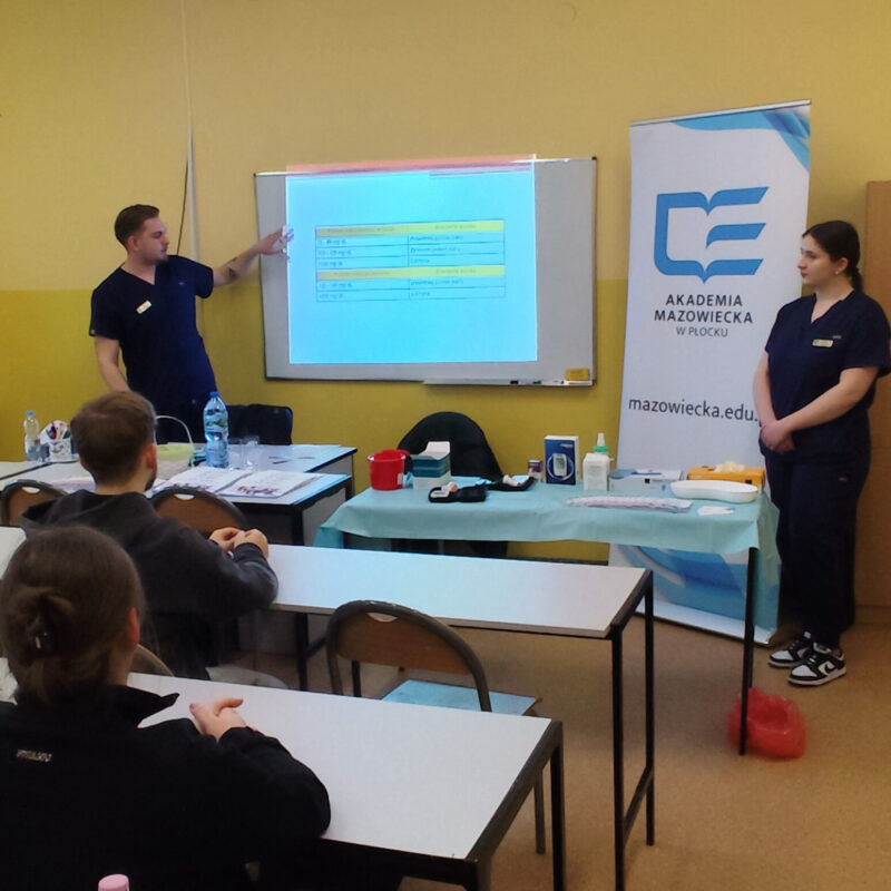 Student omawiający prezentację z podstaw oznaczania poziomu glikemii przed uczniami siedzącymi w ławkach szkolnych