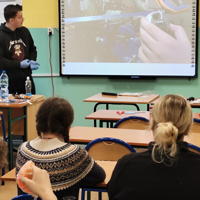 Student omawiający prezentację z kryminalistyki przed uczniami siedzącymi w ławkach szkolnych