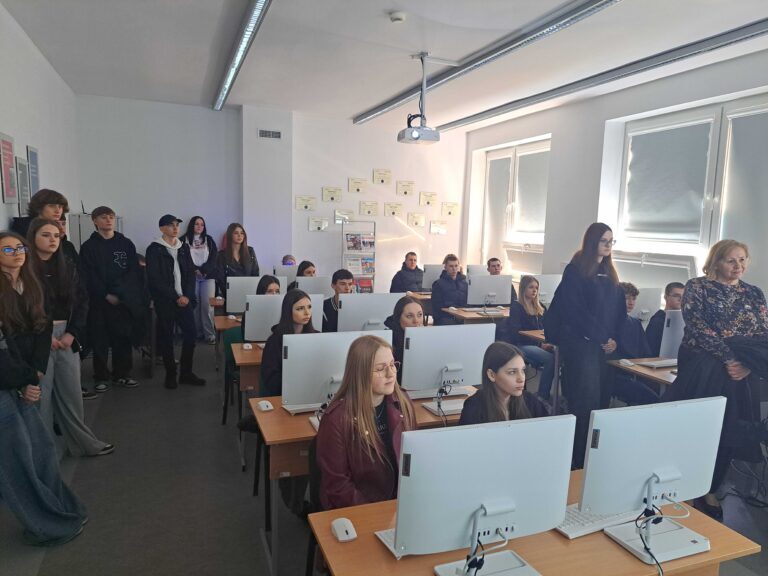 uczniowie siedzący w ławkach w sali przed komputerami