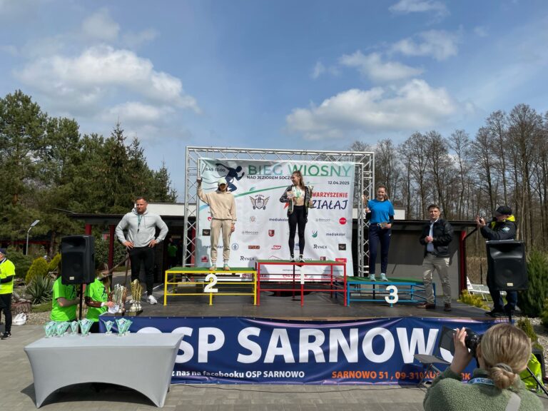 Zdjęcie podium z laureatkami pierwszych 3 miejsc w Biegu Wiosny, z tyłu za nimi ścianka promocyjna biegu