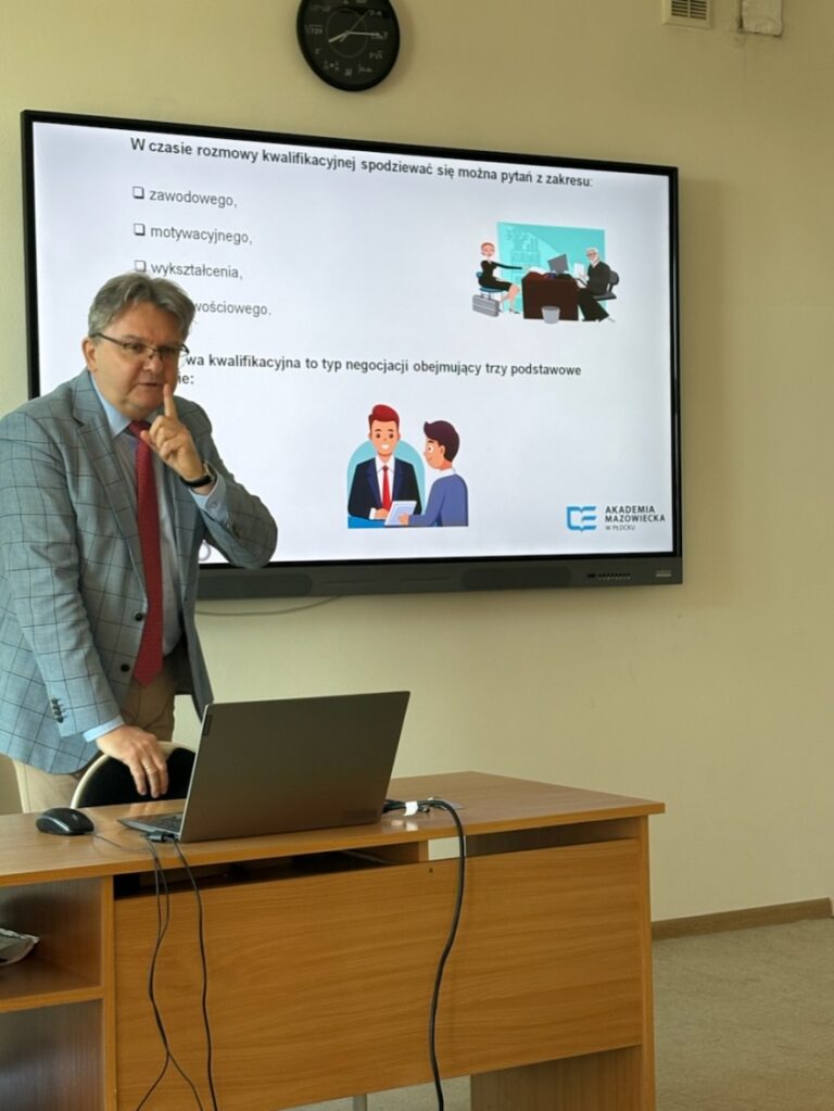 nauczyciel akademicki stojący przed ekranem z prezentacją, trzymający mikrofon