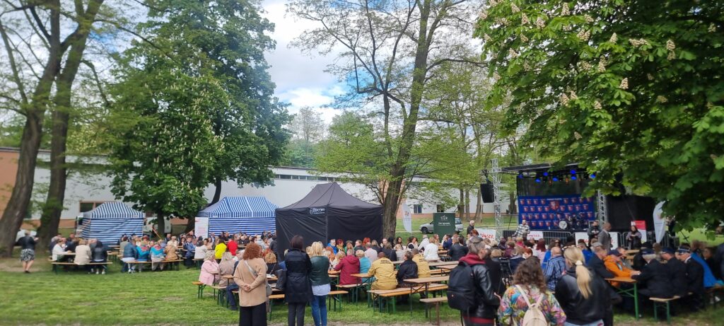 zbiorowisko ludzi siedzących na ławkach w plenerze przed namiotem