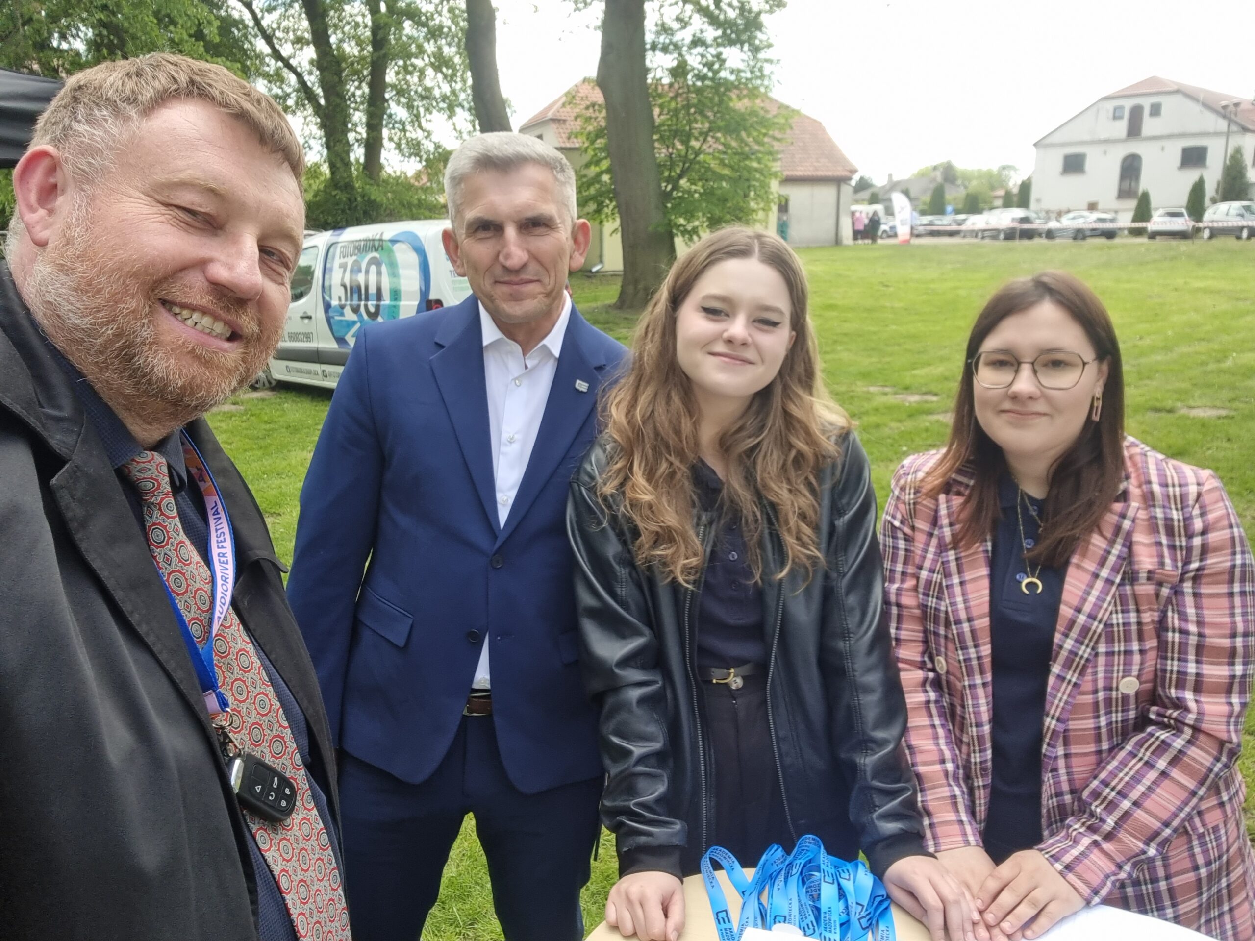 Przedstawiciele Uczelni i studentki pozujący do zdjęcia w plenerze przy ladzie promocyjnej