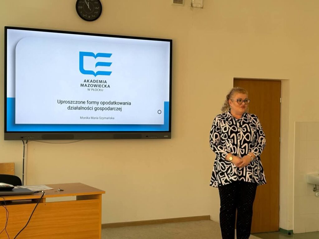 Nauczycielka akademicka, stojąca podczas wykładu w klasie, w tle ekran z prezentacją
