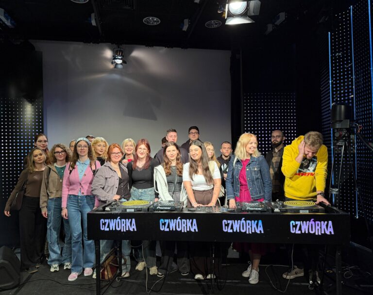 Uśmiechnięci studenci z nauczycielami akademickimi przy konsoli radiowej pozujący do zdjęcia