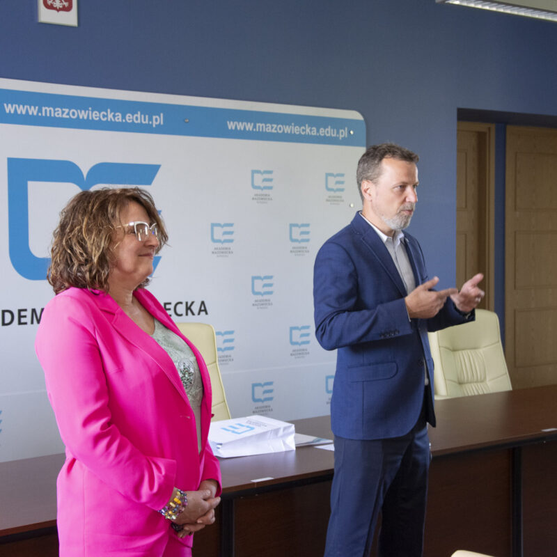 Rektor podczas rozmowy ze studentami, w towarzystwie Pani Prorektor, w tle ścianka z logotypami uczelni
