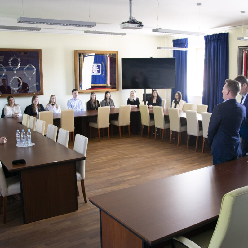 Rektor przemawiający do studentów siedzących przy stole w sali senatu