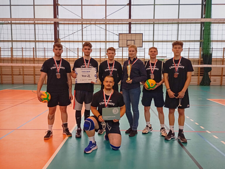 Drużyna Akademii Mazowieckiej w Płocku wraz z opiekunką pozujący do zdjecia, sześciu mężczyzn studentów i kobieta opiekunka kierownik Studium WF stojący na Hali Sportowej trzymający piłkę i dyplom