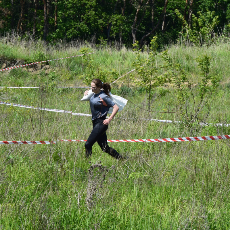 kobieta biorąca udział w zawodach biegowych, biegnąca z workiem z piaskiem na ramieniu