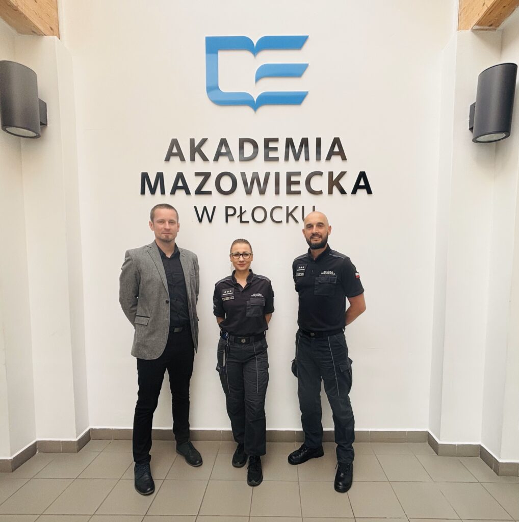 Trzy osoby, dwóch mężczyzn i kobieta pozują do zdjęcia na tle ściany z logotypem Akademii Mazowieckiej w Płocku