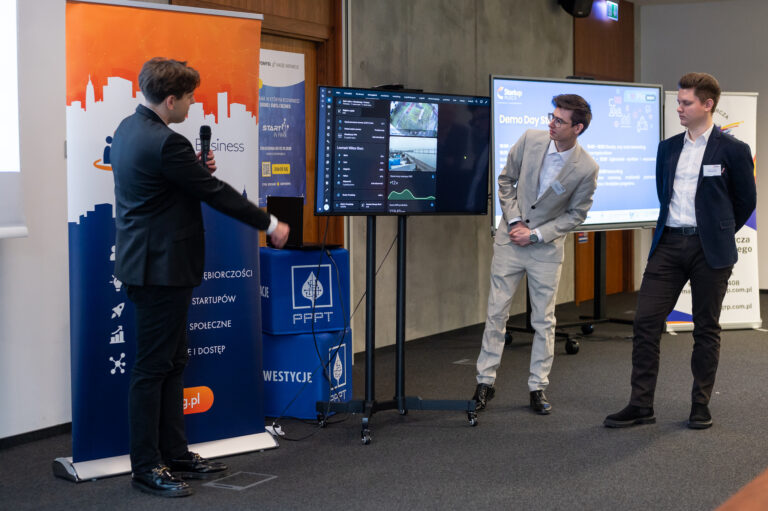 Zdjęcie 2 męzczyzn stojacych obok siebie i patrzących w ekran, trzeci z nich wskazuje coś ręką.