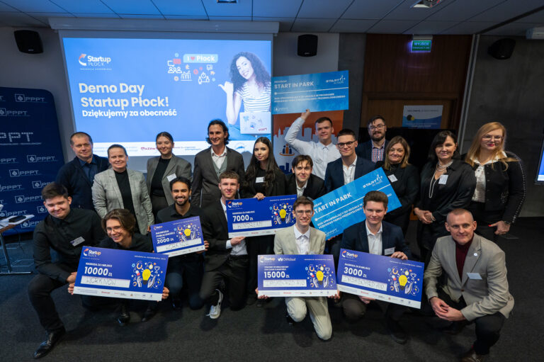 zdjęcie grupowe osób trzymających w rękach duże plansze z nagrodą, w tle ekran z prezentacją